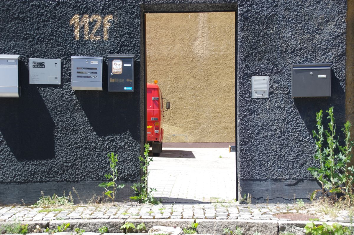 Wand mit Durchgang zu einem Hof in dem ein roter Transporter parkt